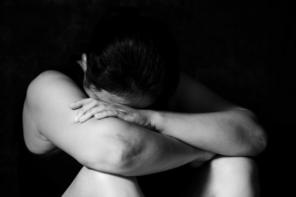 A woman sitting on the ground with her head between her knees and her arms wrapped around her seeming to be crying
