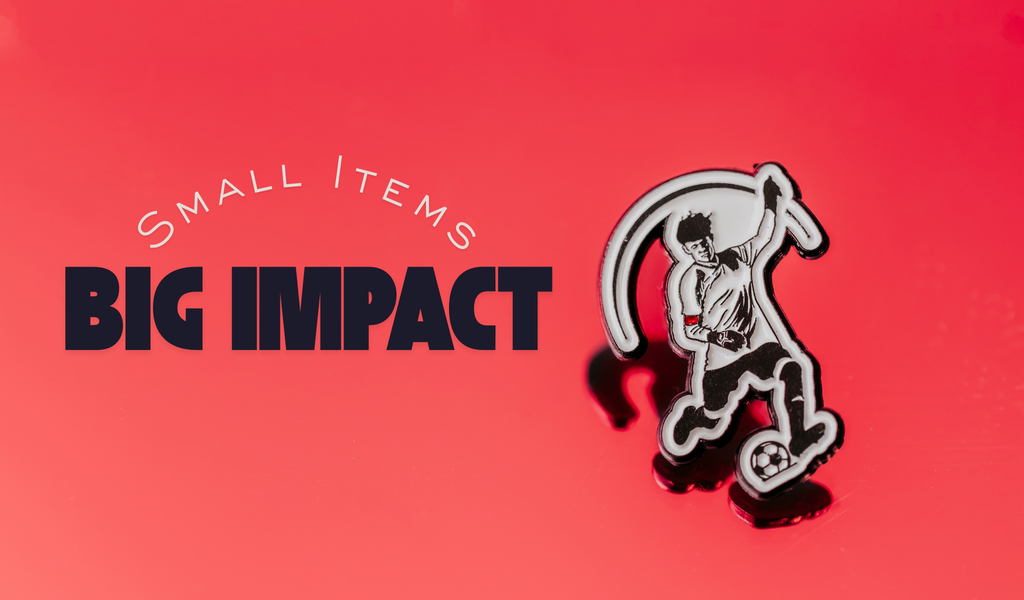 Banner graphic showing enamel pins and colorful wristbands with text that reads ‘Small Items. Big Impact.’ promoting creative fundraising ideas from Dream Maker Pins.