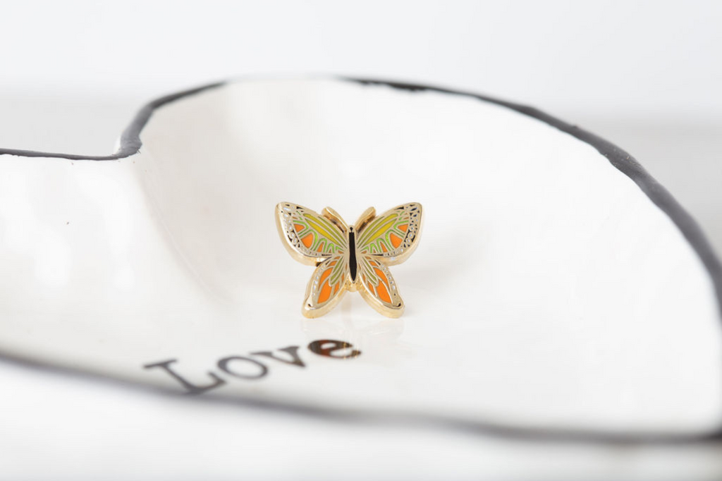 dream maker pins orange monarch butterfly enamel pin on a ring dish that says love