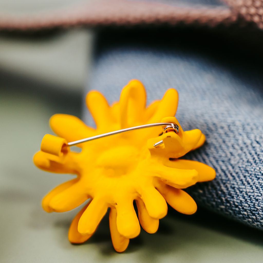Yellow sunflower-shaped brooch backside on a denim fabric background